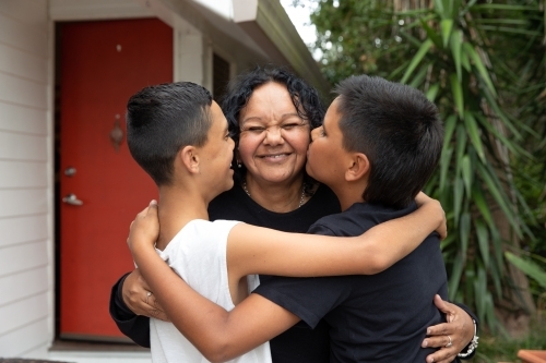 Aboriginal family hugging and kissing in backyard - Australian Stock Image