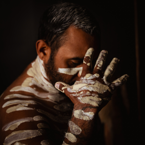 Aboriginal male painted up covering face - Australian Stock Image