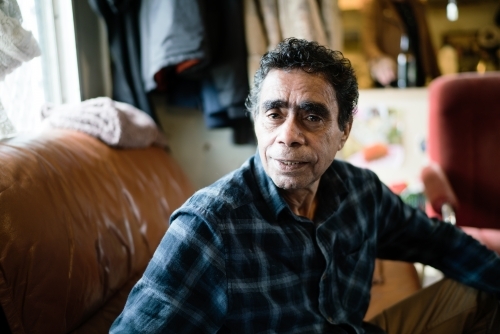 Aboriginal Man wearing plaid shirt Seated on a Couch - Australian Stock Image