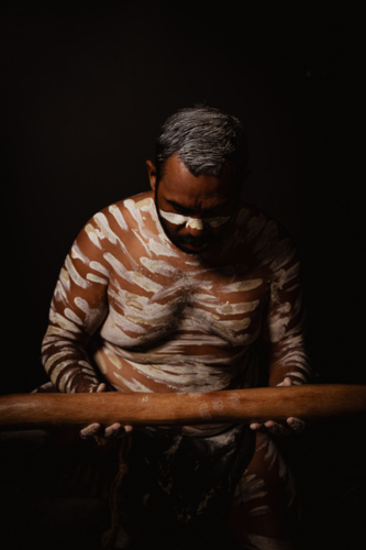 Aboriginal man with white body paint holding a wooden didgeridoo. - Australian Stock Image