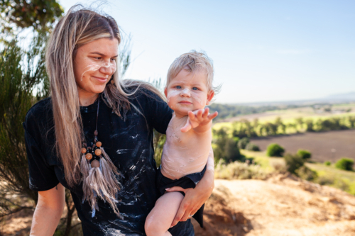 Aboriginal mum with her baby boy together by cliff on country in Australian bushland - Australian Stock Image