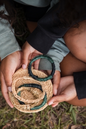 Aboriginal people sitting on grass, weaving fibre baskets and bracelets - Australian Stock Image