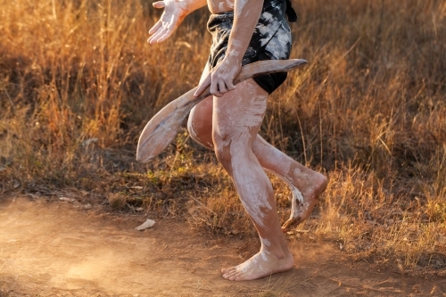 Aboriginal person dancing and telling cultural stories while holding digging and hunting stick - Australian Stock Image