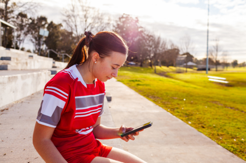 aboriginal teen girl football player using mobile phone device - Australian Stock Image