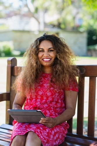 aboriginal woman on park bench, using ipad - Australian Stock Image