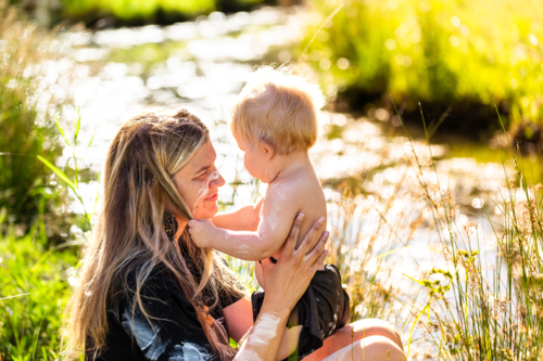 Aboriginal woman with her young child together in Australian bushland by sparkling creek water - Australian Stock Image