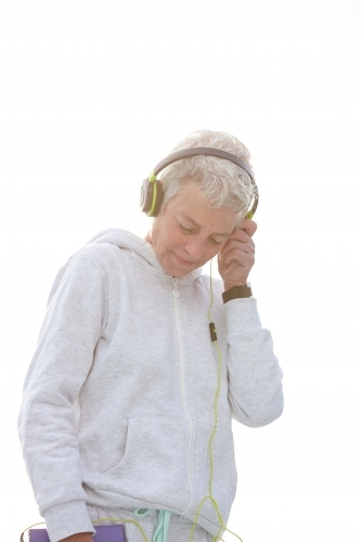 Active senior lady listening to music with headphones - Australian Stock Image