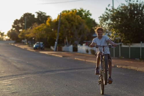adolescent boy riding bicycle on quiet street with no helmet - Australian Stock Image
