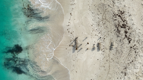 Aerial of old jetty posts in the sand at a beach - Australian Stock Image