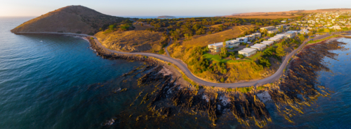 Aerial panorama of a winding coastal road around a rocky headland and housing community - Australian Stock Image