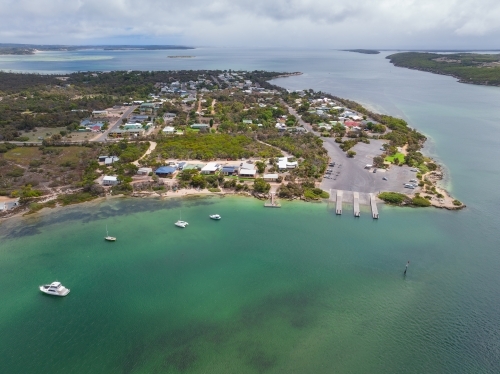 Aerial view of a boat ramp at a small coastal town alongside a calm ocean bay - Australian Stock Image