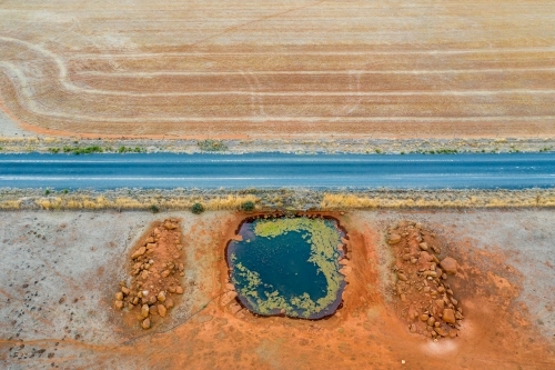 Aerial view of a country road next to a dam on dried farmland.