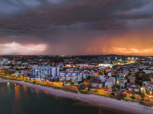 Aerial view of a dramatic thunderstorm advancing over apartment buildings along a coastal esplanade - Australian Stock Image