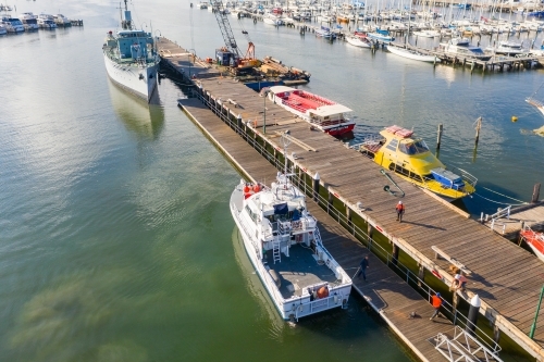 Aerial view of a naval ship at a dock at a bay side harbour - Australian Stock Image