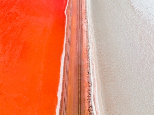 Aerial view of a railway line running across a salt lake with one side vivid red in colour - Australian Stock Image