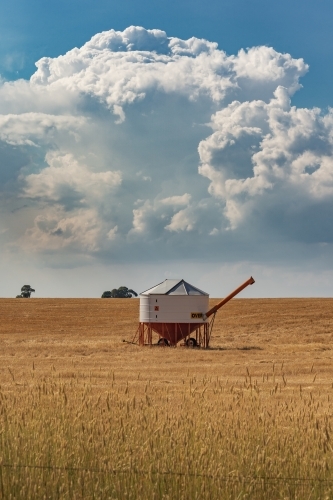 Aerial view of a solitary field bin sitting in a large barren paddock under a large storm cloud - Australian Stock Image