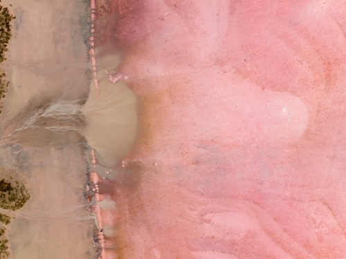 Aerial view of brown silt draining on to a pink salt lake - Australian Stock Image