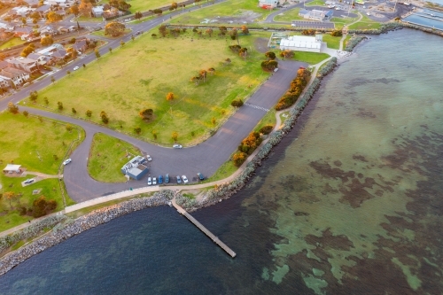 Aerial view of coastal reserve and parkland with a small jetty next to a calm bay - Australian Stock Image
