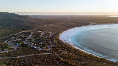 Aerial view of crescent-shaped beach at sunset with caravan park stop - Australian Stock Image