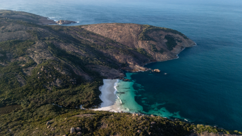 Aerial view of crescent-shaped beach with turquoise water against rugged headland - Australian Stock Image
