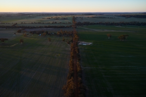 Aerial view of farmland, with cropped fields, a dam and a gravel road in the fading evening light. - Australian Stock Image