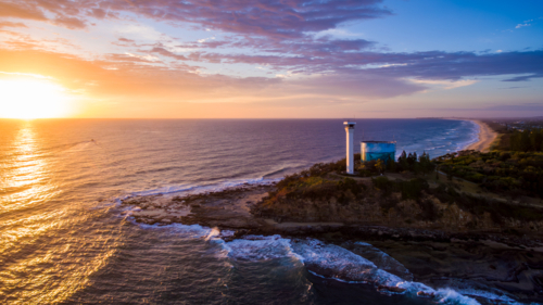 Aerial view of Point Cartwright lighthouse and water tank reservoir at sunrise. - Australian Stock Image