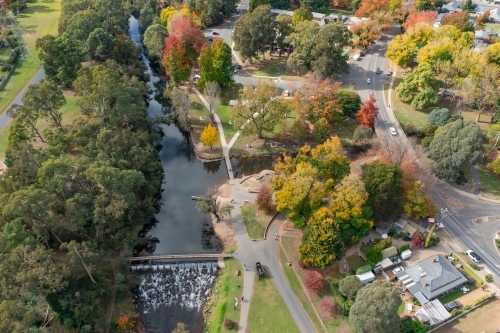 Aerial view of river running through a regional town full of Autumn coloured trees - Australian Stock Image