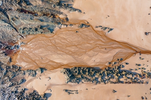 Aerial view of tannin stained creek spreading out over a sandy beach - Australian Stock Image