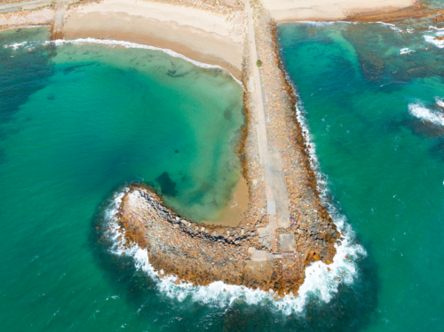 Aerial view of waves breaking on a long rocky breakwater - Australian Stock Image