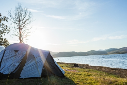 Afternoon Sun flare over tent pitched by edge of Lake St Clair in Hunter Valley - Australian Stock Image