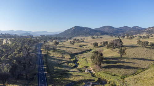An aerial scene of a country highway, green fields and mountains in the distance - Australian Stock Image