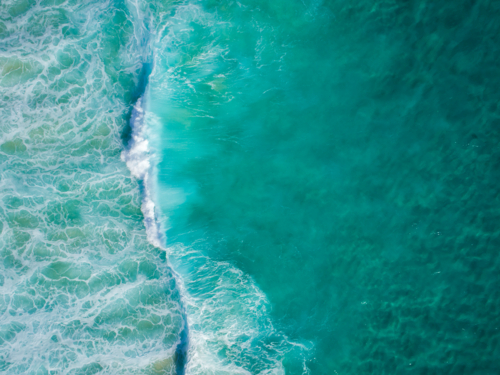 An aqua blue wave travels along crystal clear water - Australian Stock Image