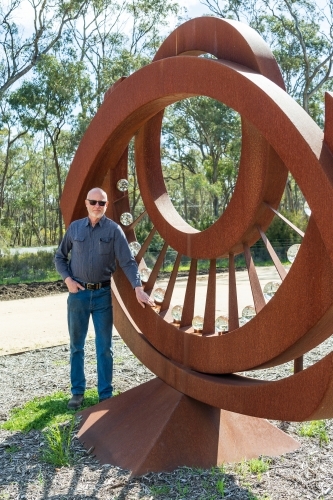 An artist standing proudly in front of a large metal sculpture - Australian Stock Image