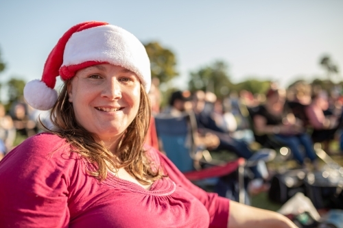 An Australian caucasian woman wearing a Santa hat at outdoor Christmas carols in the summer - Australian Stock Image