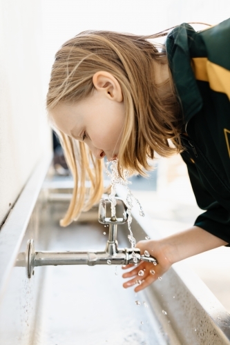 An Australian primary school girl drinking out of a water tap bubbler in the school yard at recess - Australian Stock Image