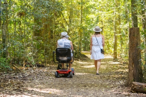 An elderly woman on a disability scooter with her daughter walking through a rainforest - Australian Stock Image