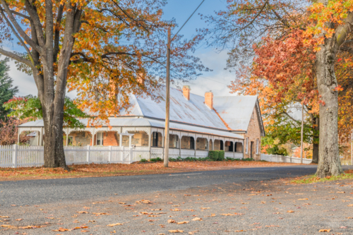 An old country home with peaked roof and white picket fence with autumn colours - Australian Stock Image
