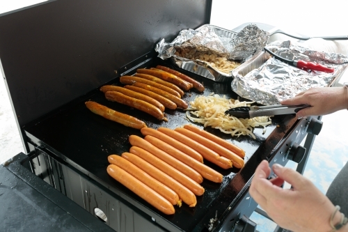 An unrecognisable person cooking a traditional australian bbq sausage sizzle, sausages cooking - Australian Stock Image