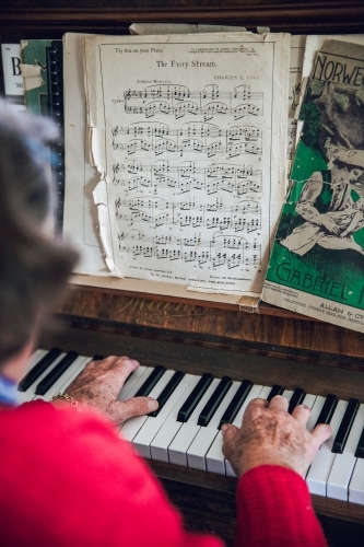 Anonymous old lady playing the piano with sheet music, wearing a red cardigan - Australian Stock Image