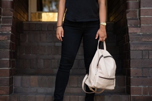 anonymous woman holding bag outside entrance to brick building - Australian Stock Image