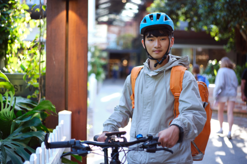 Asian delivery rider walking with his bicycle - Australian Stock Image