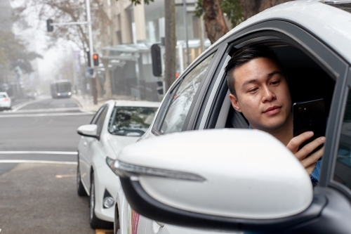 Asian man parked in car checking mobile phone - Australian Stock Image