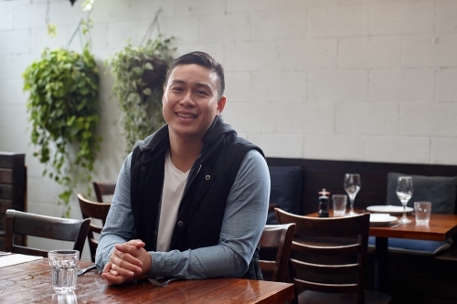 Asian man sitting at table at restaurant - Australian Stock Image