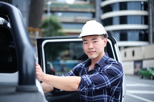 Asian man with hard hat getting into car - Australian Stock Image