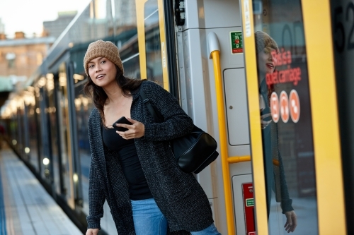 Asian woman at train station with mobile phone - Australian Stock Image