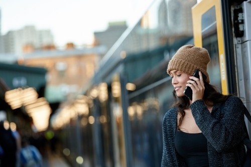 Asian woman getting off train at station talking on mobile phone - Australian Stock Image