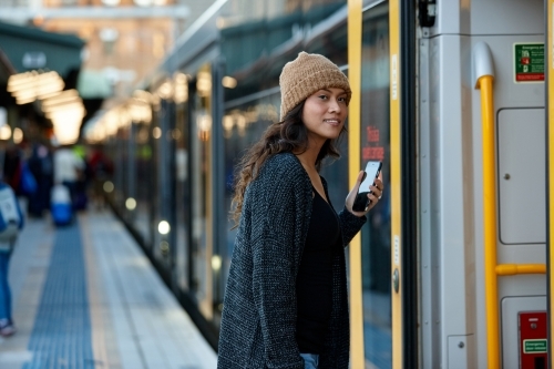 Asian woman getting on train with mobile phone - Australian Stock Image