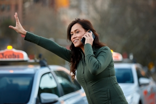 Asian woman hailing taxi with mobile phone - Australian Stock Image