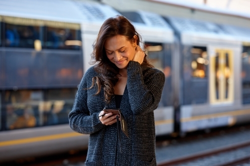 Asian woman smiling whilst waiting at train station with mobile phone