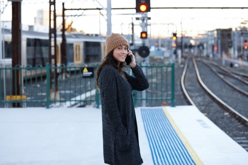 Asian woman waiting at train station talking on mobile phone - Australian Stock Image